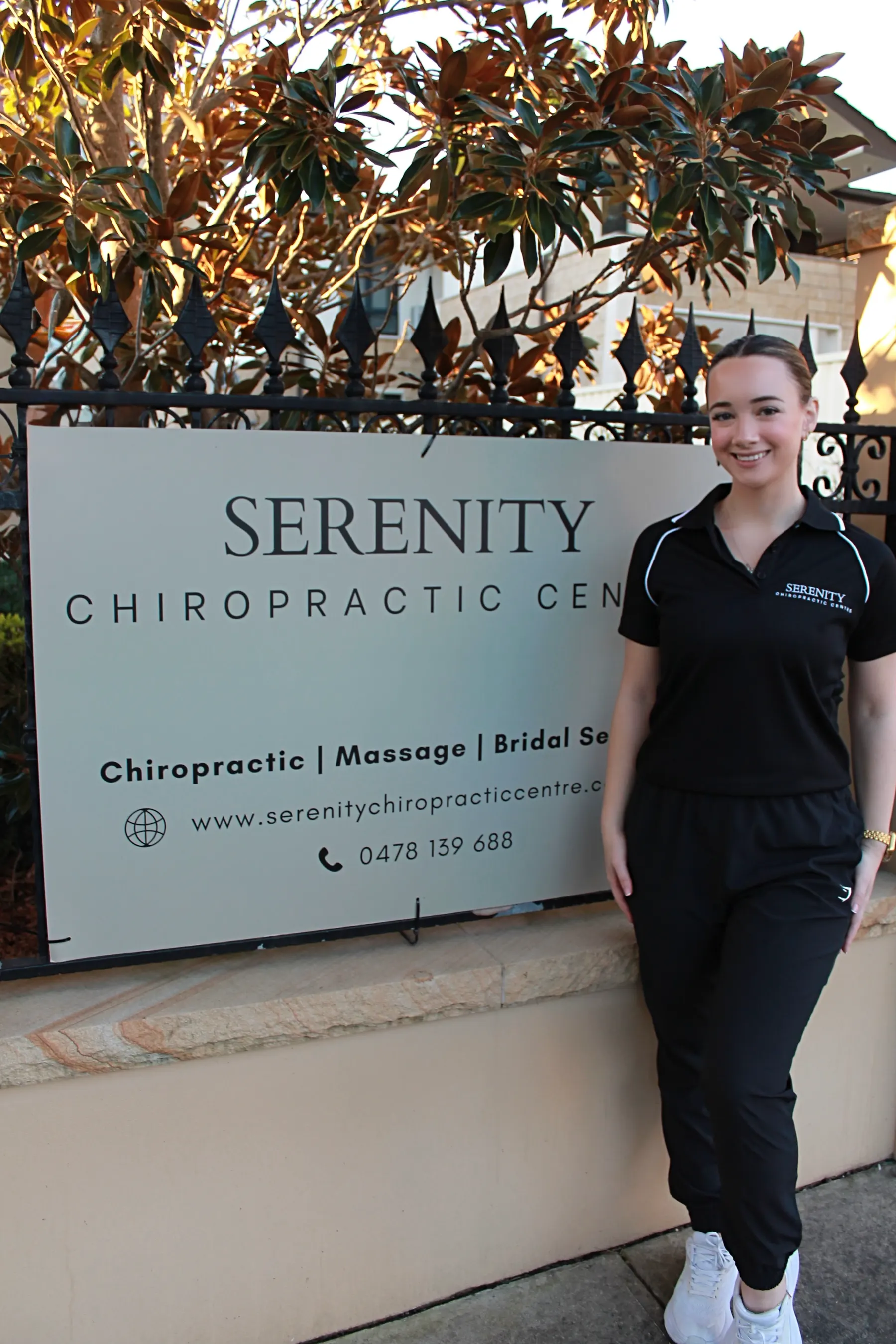 Alicia Neil standing beside the Serenity Chiropractic Centre sign